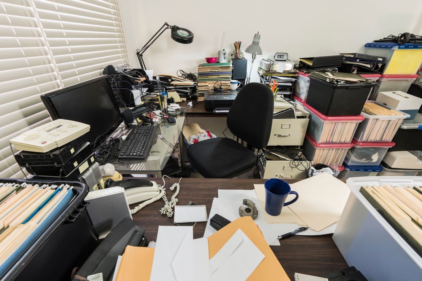 A cluttered office desk buried in paper files, folders and loose documents